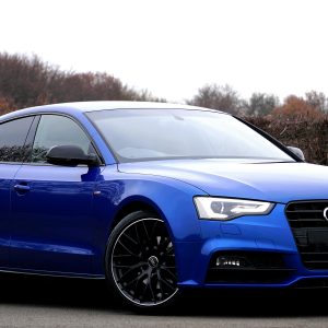 Elegant blue luxury car parked outdoors against a natural backdrop.